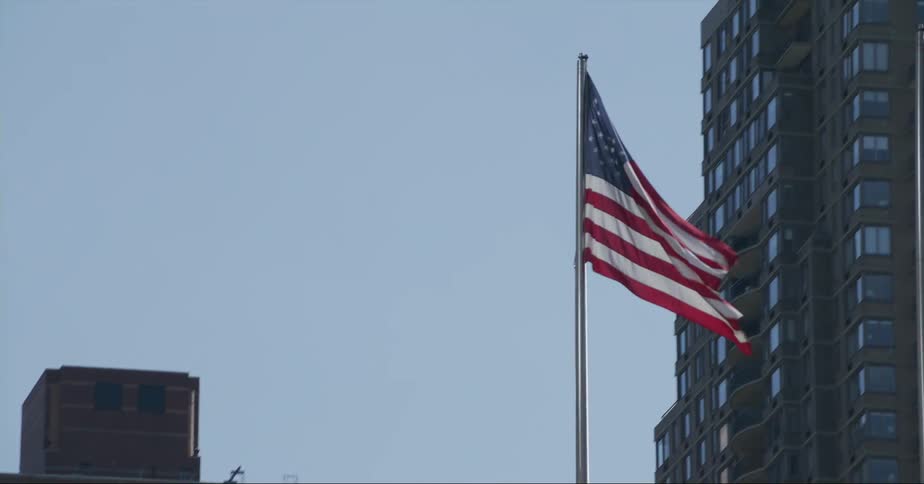 An american flag waves atop a pole in a city during the day