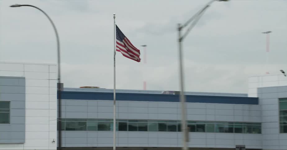 An american flag waves on a pole near highway traffic and the airport