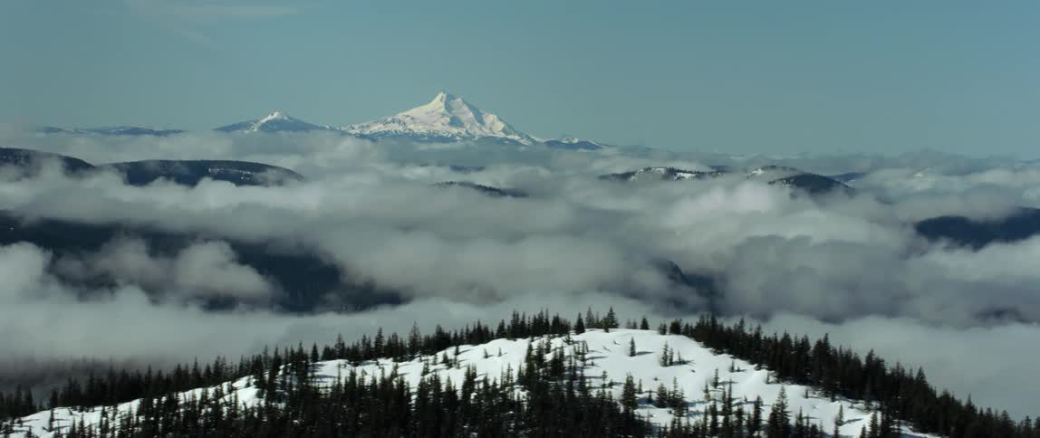 A snow capped mountain peak looms over a mountainous countryside obscured by fog