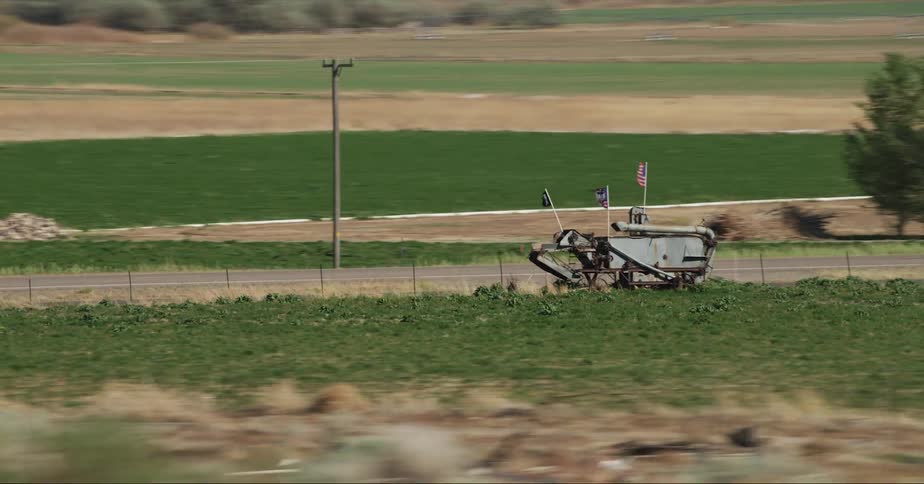 An american flag flies on a piece of farming equipment near crop fields