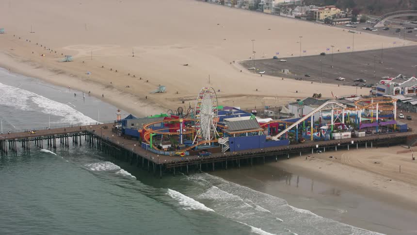 An amusement park sits on a pier on the beach of a large city