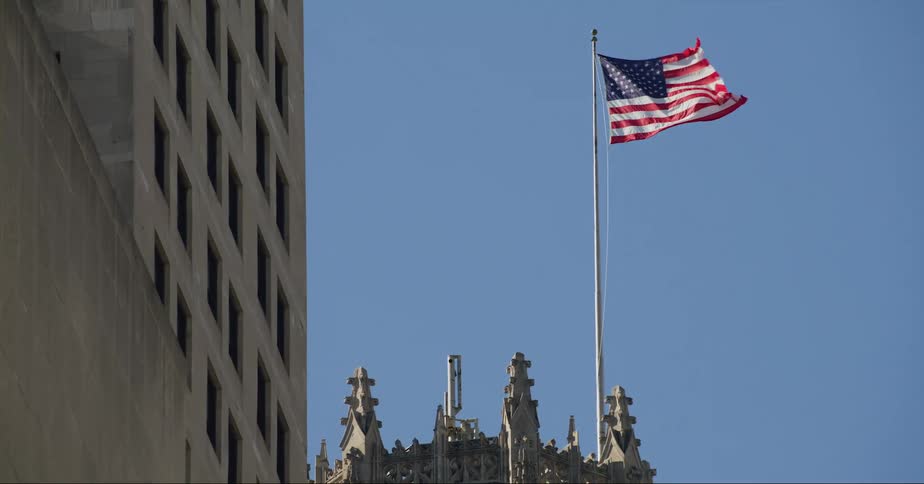An american flag waves on a pole atop a building in a city on a clear day