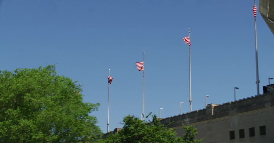 Several american flags sit on government building under a clear blue sky