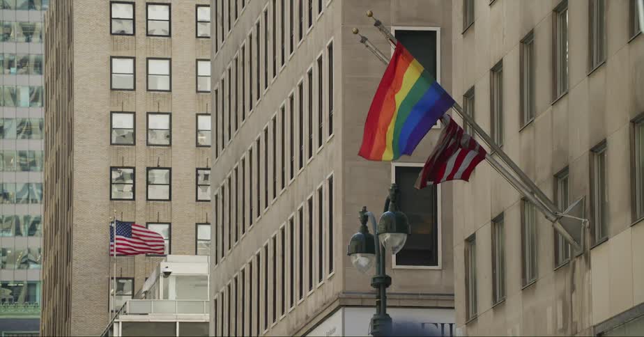 Flags wave atop poles mounted on the facade of a building in a city during the day