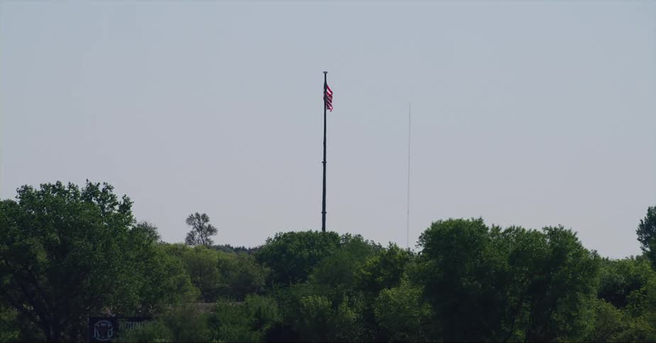 An american flag waves in the wind on a pole high above the trees