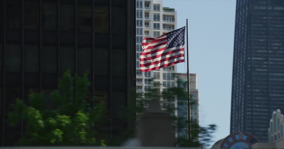 An american flag waves atop a pole outside a building in a metropolis during the day
