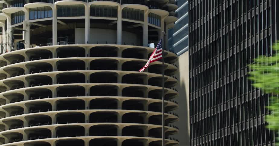 An american flag waves atop a pole outside a building in a metropolis during the day