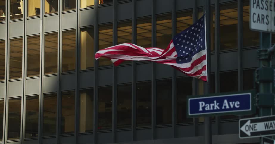 Traffic passes by as an american flag flies in front of a building on park avenue