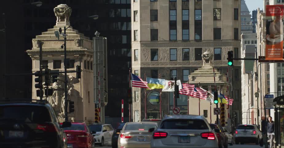 Cars move along street through downtown passing series of flags