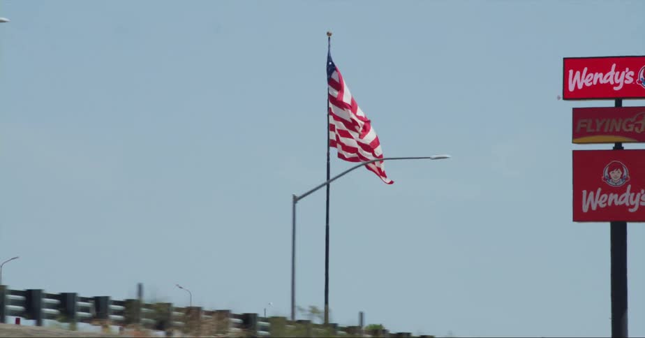An american flag waves in the breeze on a pole along the roadside near signs