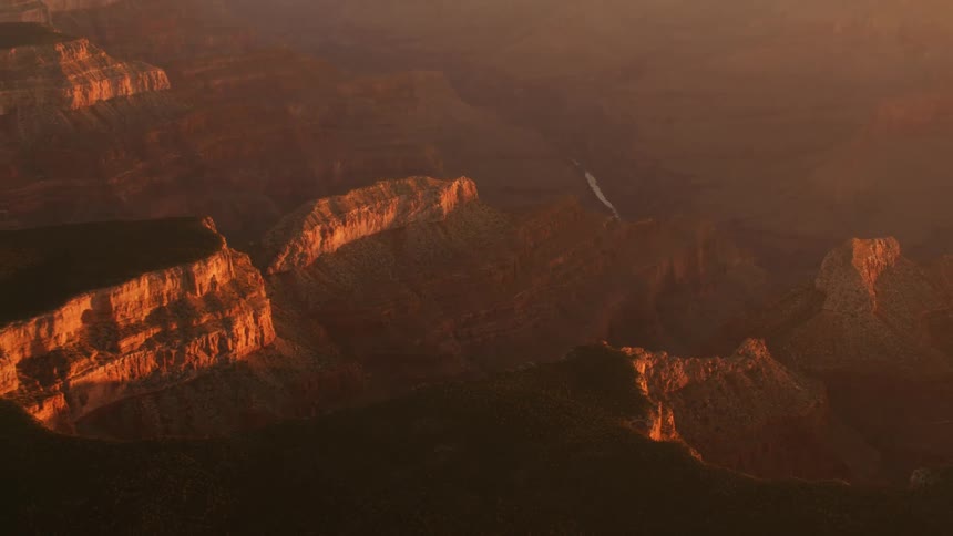 Red tinted mist fill valley as river flows through badlands past dark plateaus and brightly lit cliff sides