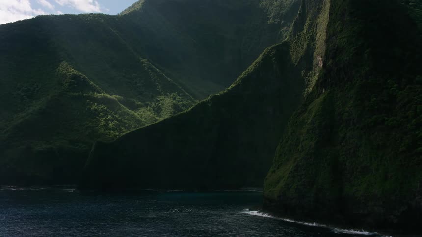Ocean waves splash against the green cliff coast on a bright day