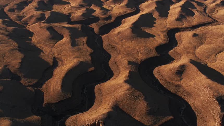 Shadowed canyons with rivers run through sandstone badlands toward edge of cliff