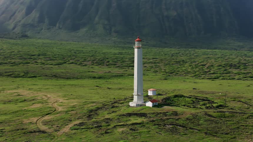 A single lighthouse tower stands amidst a grassy field near an ocean coastline