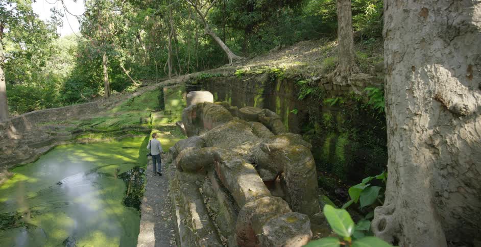 A man walks near the water by a statue