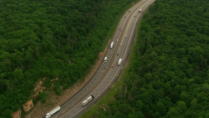 Shipping trucks travel along a freeway through a vast forest during the day