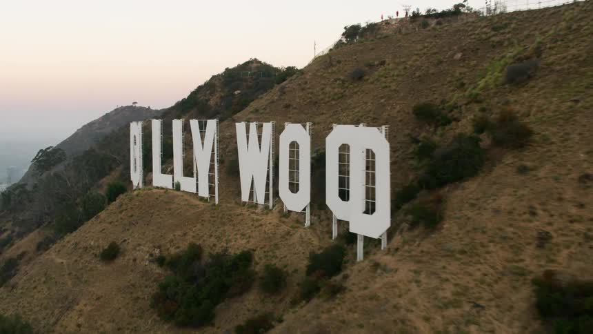 Hollywood sign sits on hill near fog covered city under a red tinted horizon