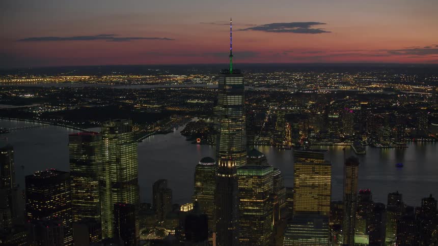 City lights glow as the sun sets and tall buildings and skyscrapers stand tall over the harbor