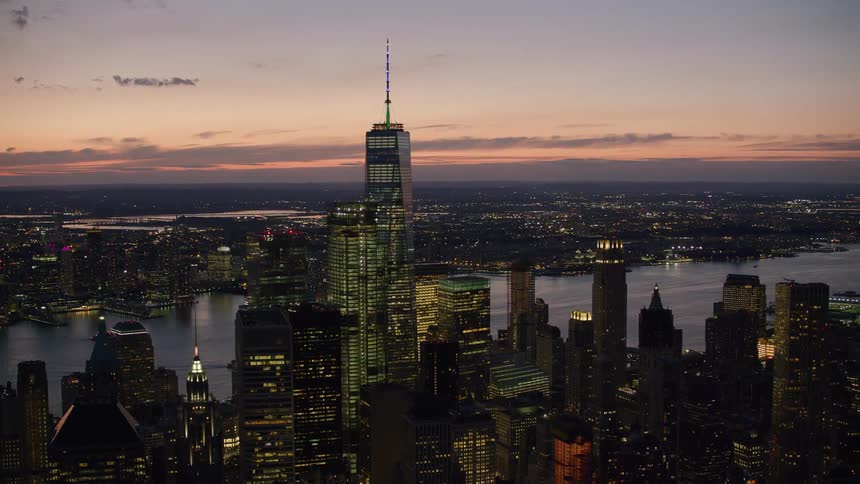 City lights glow as the sun sets and tall buildings and skyscrapers stand tall in the harbor