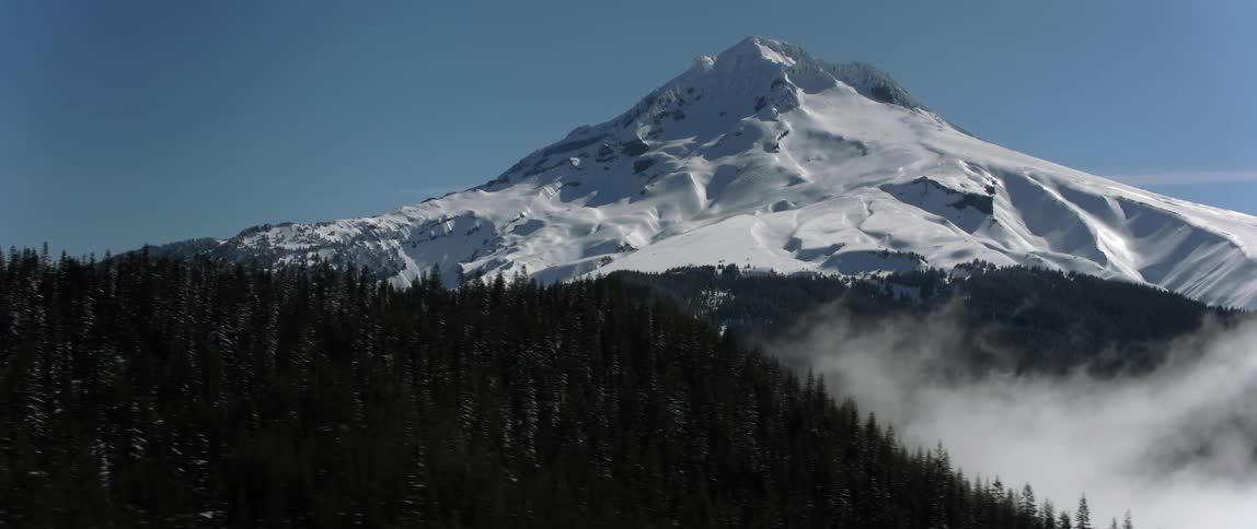Fog and low clouds hang over the trees with the snow capped peak of mount hood above
