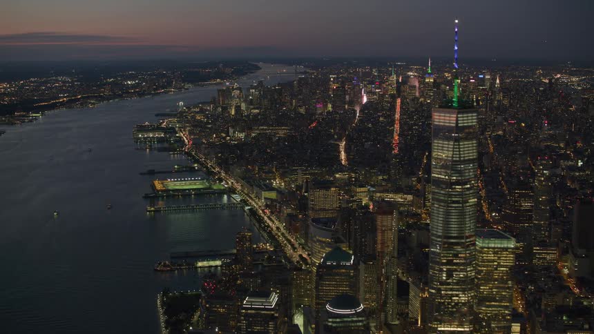 The spire on one world trade center is colorfully lit as it stands tall near the waterfront in new york