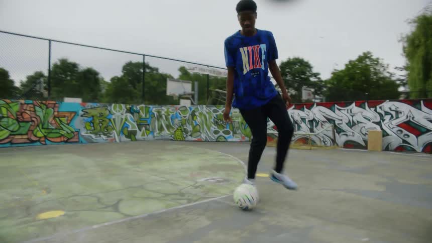Youth dribbles soccer ball practicing on park sports court with graffiti painted walks