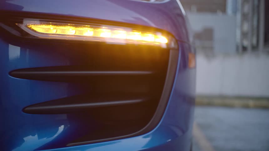 The front turn blinker light of a blue car flashes once as its parked in a parking space