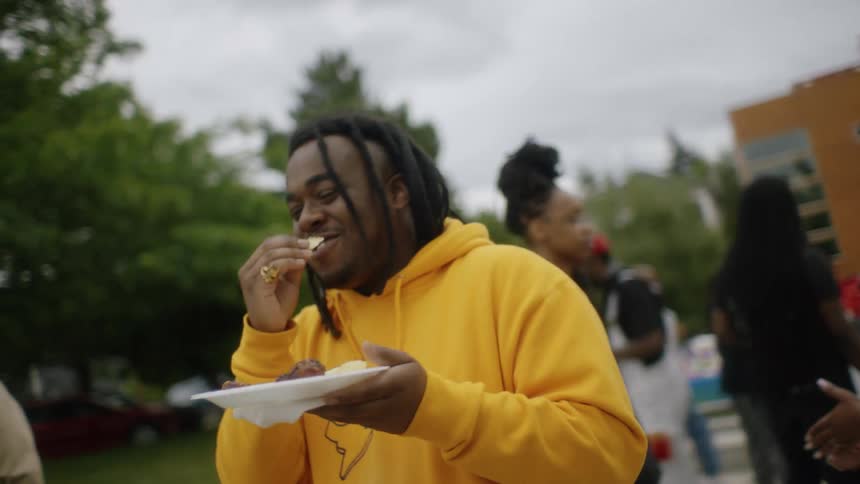A man laughs while eating at a cookout in a park