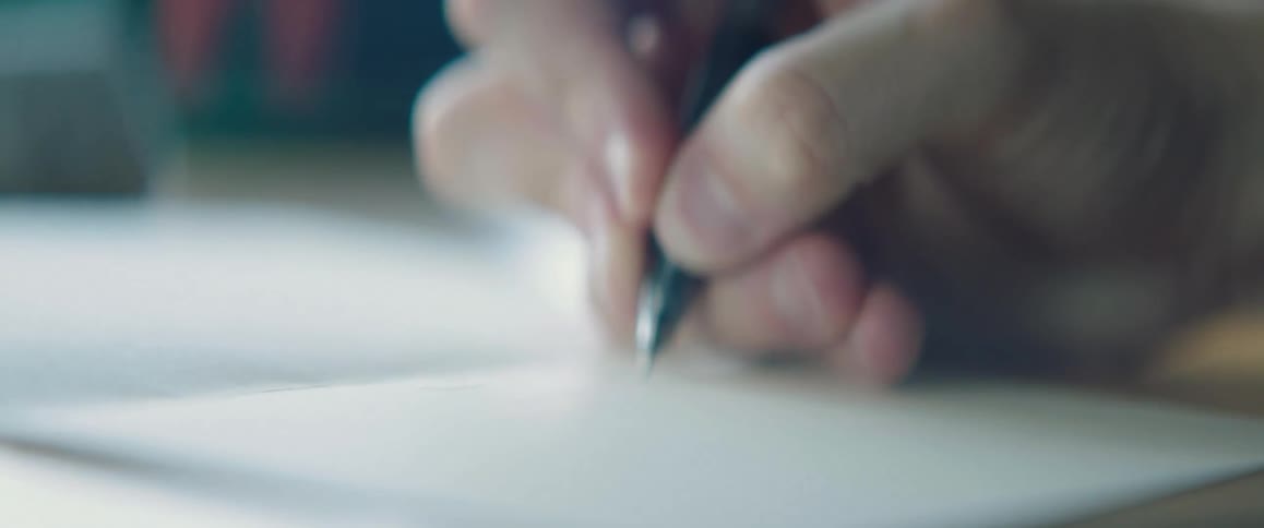 A hand holding a pen sketching on a blank page in a notebook