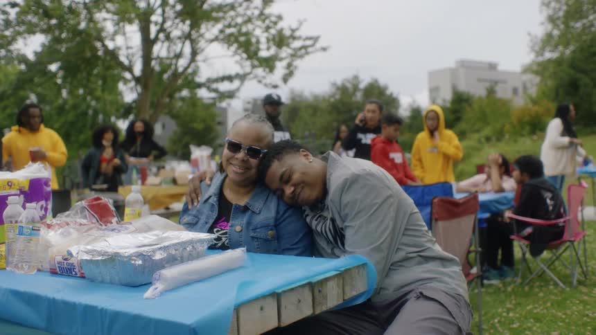 A man sits down and hugs his mom during a cookout