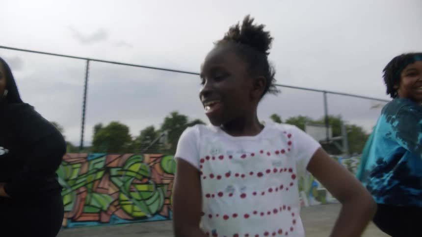 A girl leads others in dance steps at the playground all laughing and smiling