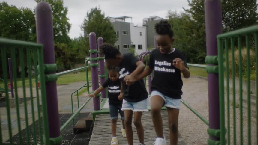 A group of children hold hands while running across a suspension bridge on a playground