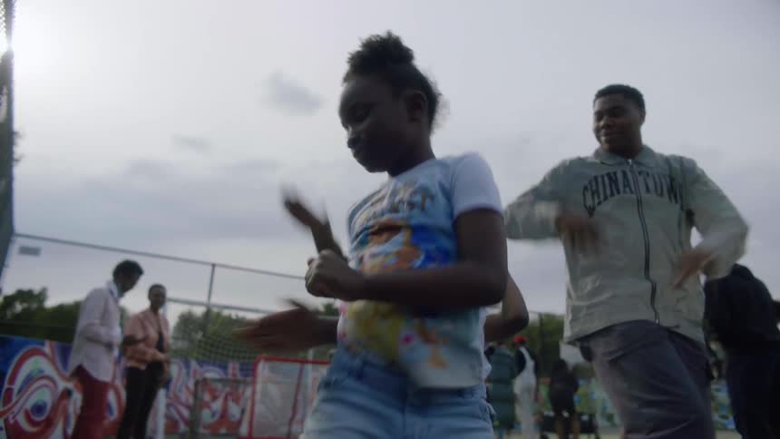 A teenage boy smiles as he tries to follow the dance steps of two little girls at the park