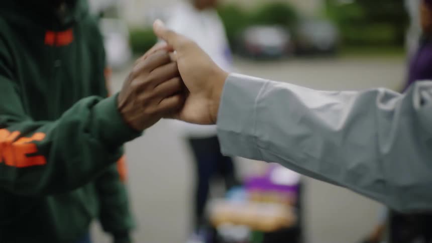 Two men greet each other with an elaborate handshake in a parking lot