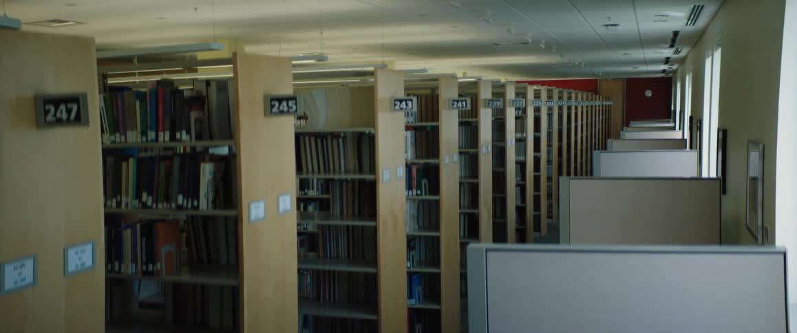 An empty library with numbered book shelves with books and a row of reading desks