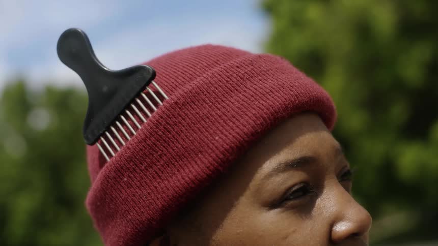 A woman stands outside with a hair pick sticking out of her hat