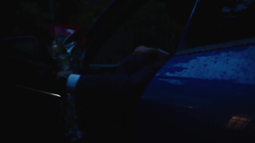 A man gets out of a car holding a bouquet of flowers