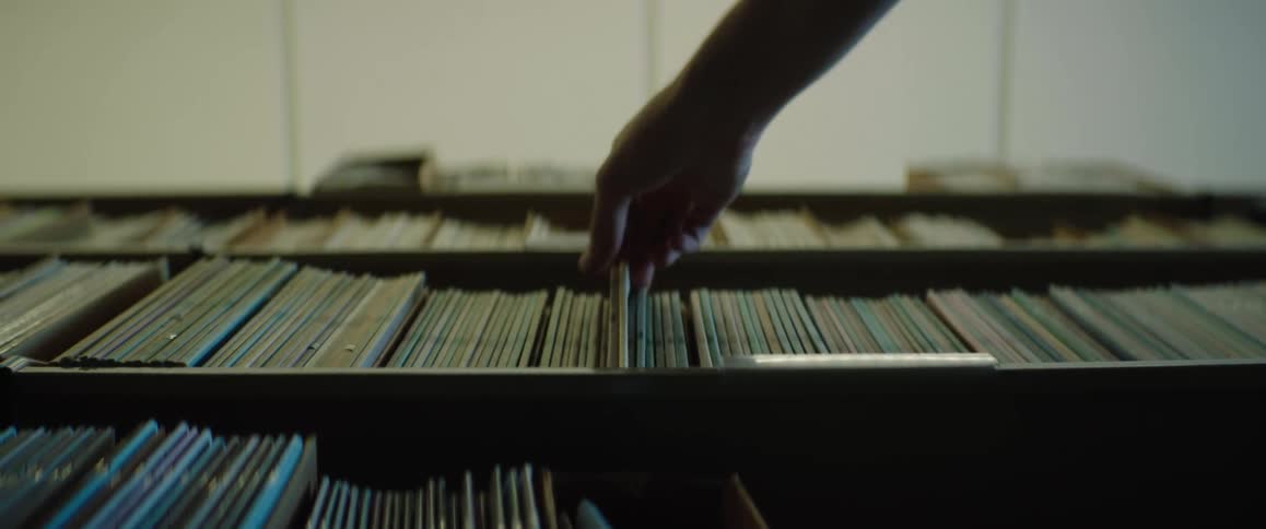 A hand moves along a library shelf then pulls out several soft cover thin books