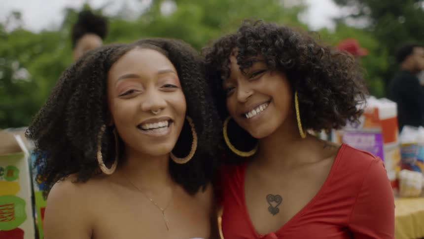 Two women laugh while standing in front of a food table during a cookout at a park