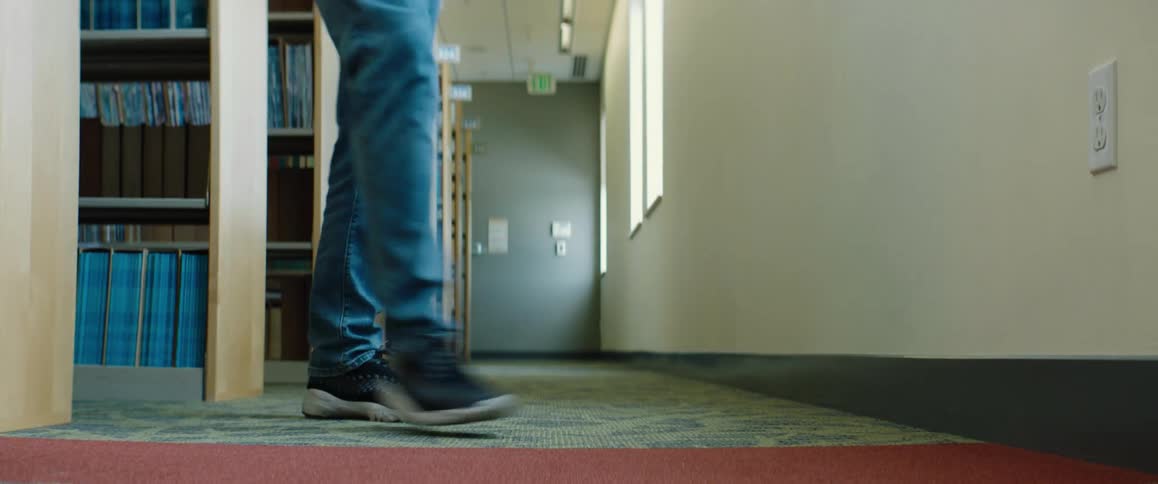 Person wearing jeans walks in and out of aisle in library