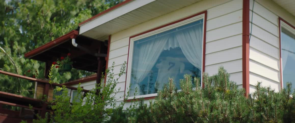 A man in a house window holds up a number 7 baseball jersey and shows it to the outside