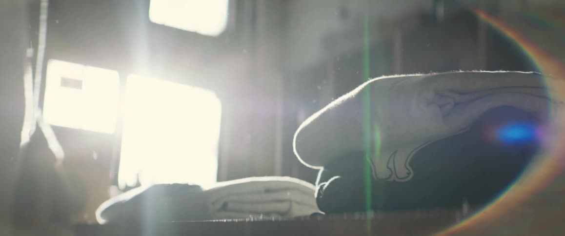 A man places a folded sweatshirt on top of another with sunlight streaming in through a window