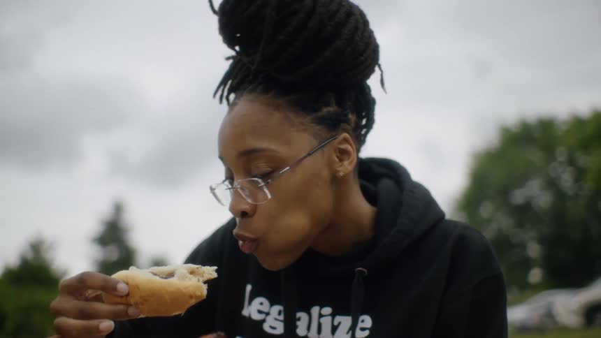 Woman poses while eating hot dog in park