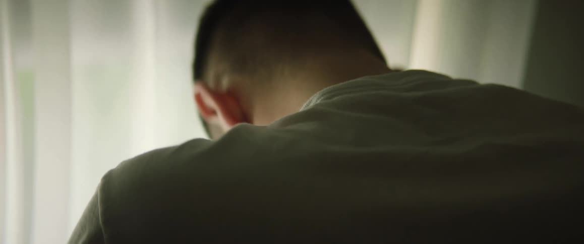 A man sitting looking out a window hangs his head in despair