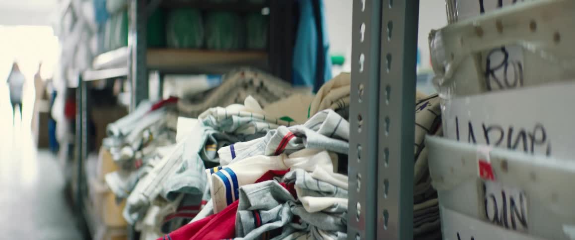 Metal shelves in a storeroom are stacked with clothing items and bins