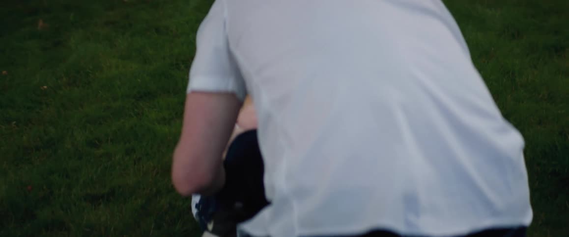A man wearing a red cap is outside playing with his young son in the yard and tickling him