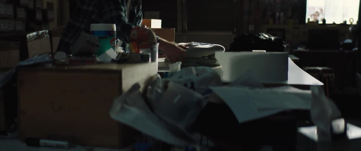 A man is folding some fabric on a table in a messy room full of items