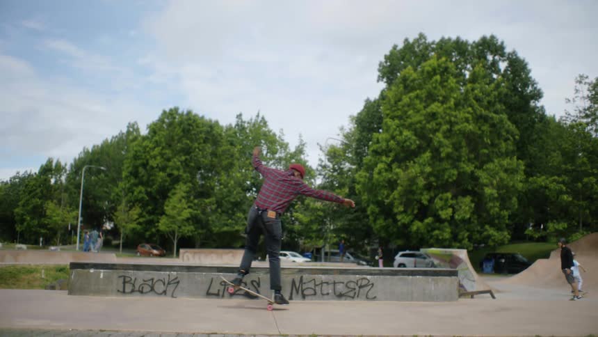 Skateboarders skate over concrete in park near graffiti of social movement slogan