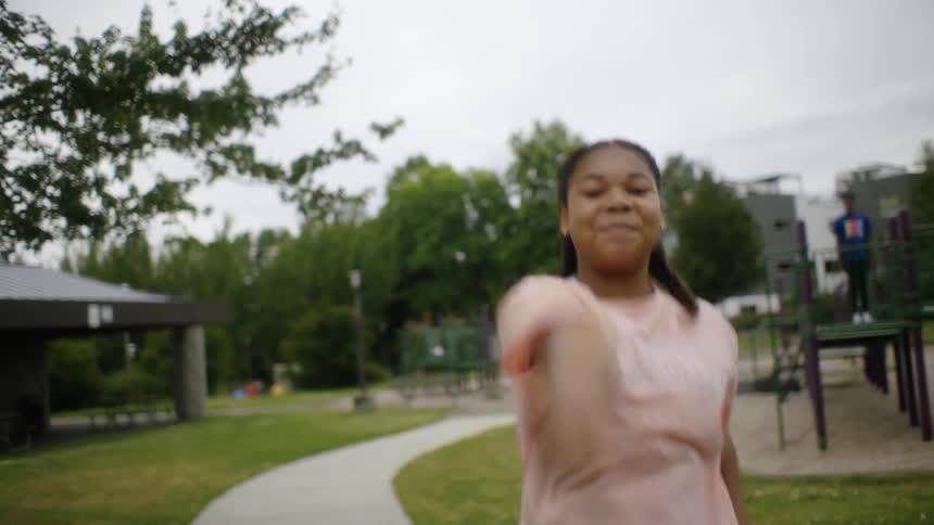 A teenage girl dances in front of a group of people at a public park