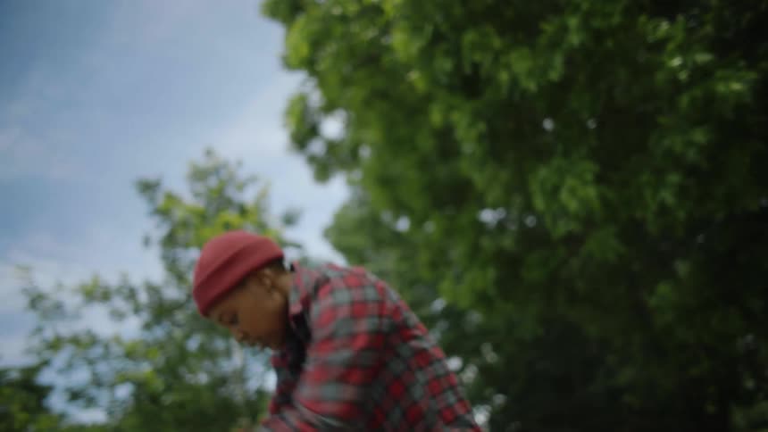 Woman with red beanie plaid shirt and gray pants rides on skateboard and performs trick in skatepark